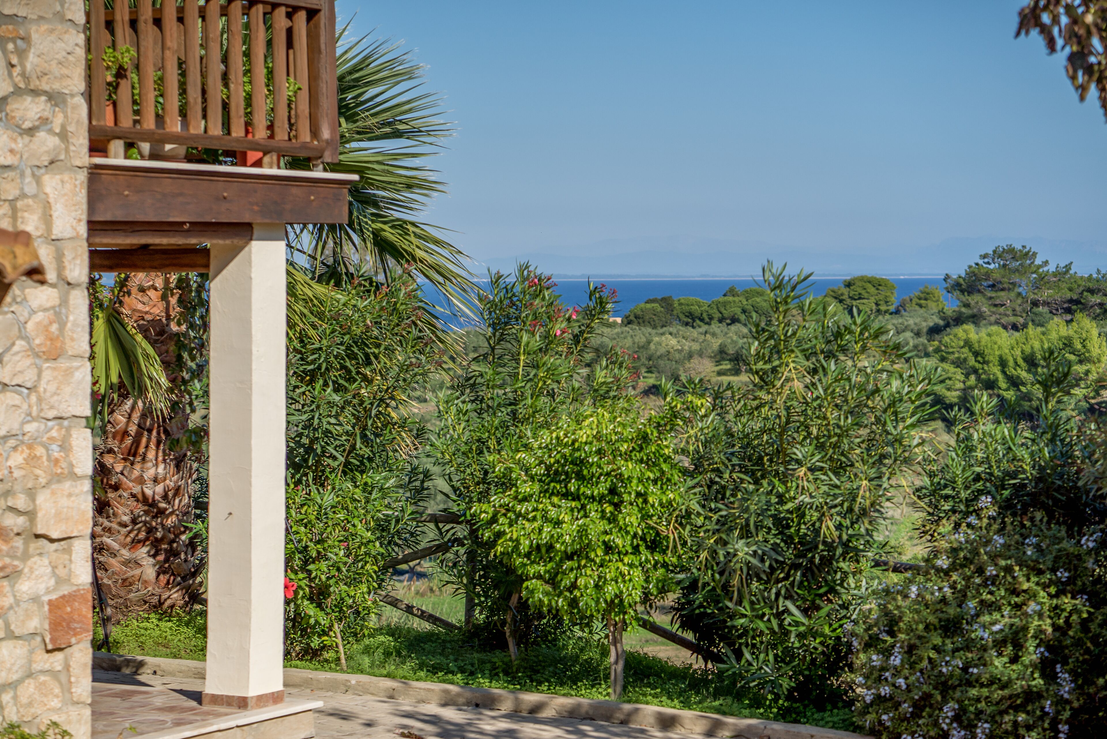 A stone building with a wooden balcony overlooking a lush landscape and the sea.