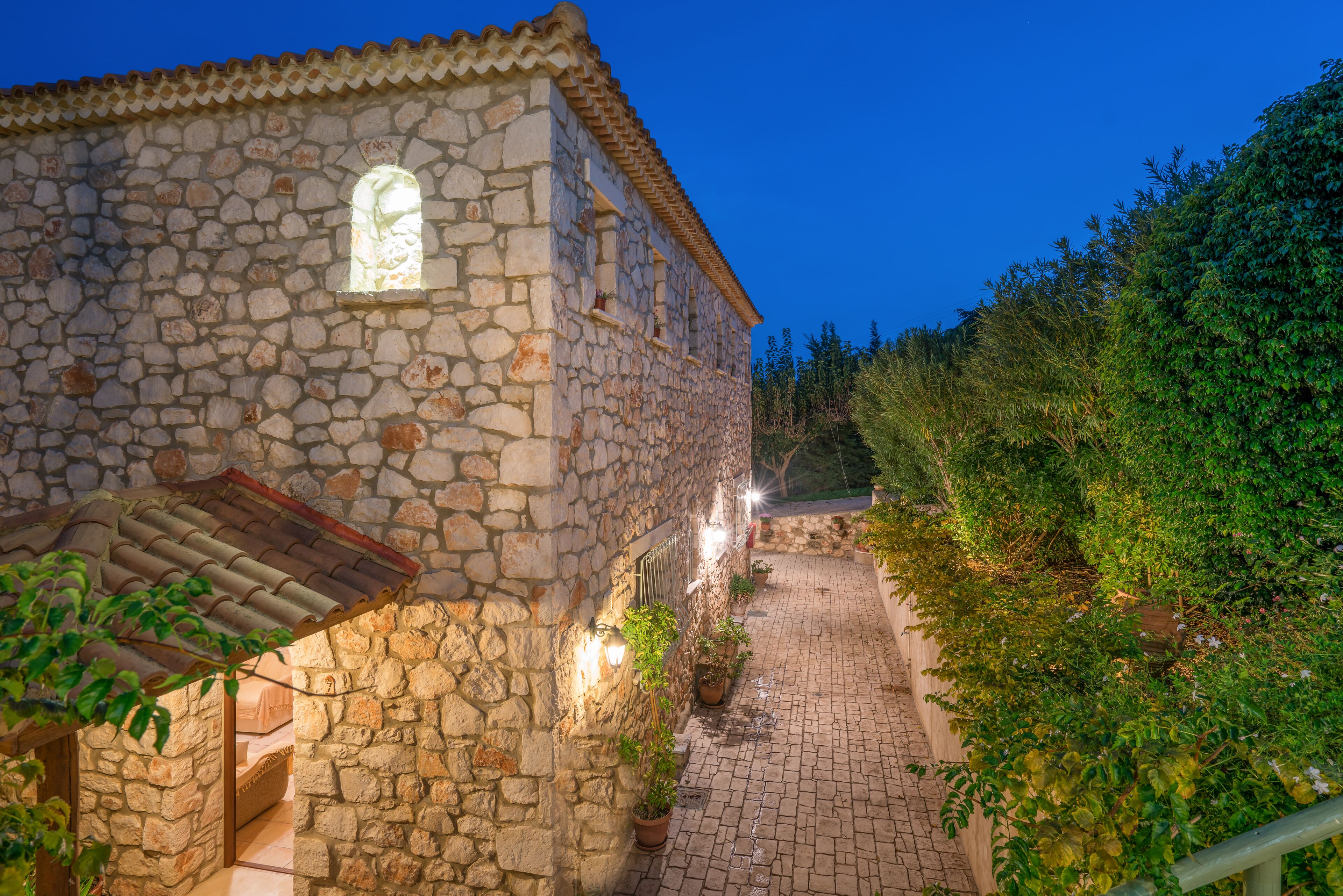A stone building with a tiled roof, a narrow pathway, and potted plants along the path.