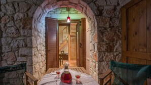 A stone-walled room with a wooden table set for two, a bottle, and glasses. - Myrties stone houses (Zakynthos)