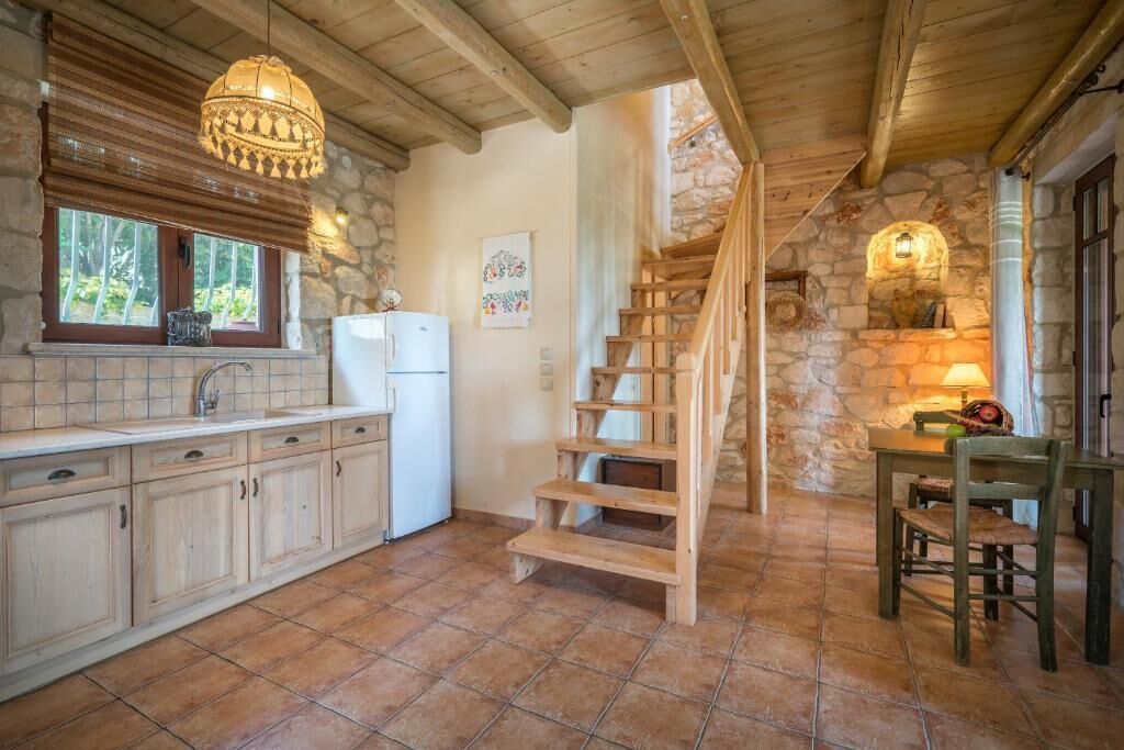 A rustic kitchen with a stone wall, wooden staircase, and a dining area with a table and chairs.