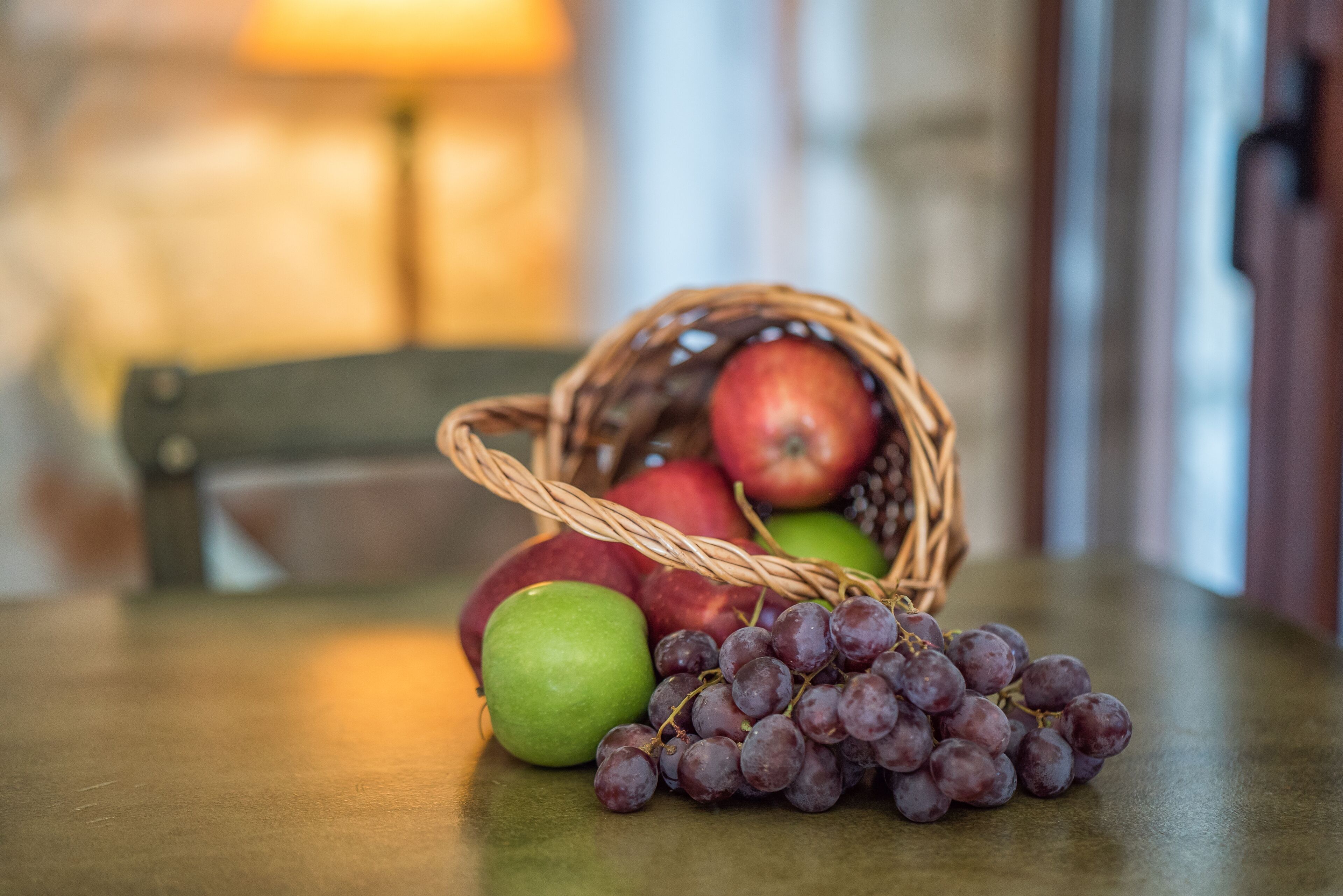 Un panier en osier contenant des pommes et des raisins, posé sur une table en bois.