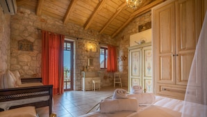 A bedroom with a stone wall, wooden ceiling, a bed with white linens, a dresser, and a wardrobe. - Myrties stone houses (Zakynthos)