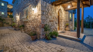 A stone building with a wooden pergola entrance, potted plants, and a cobblestone pathway. - Myrties stone houses (Zakynthos)