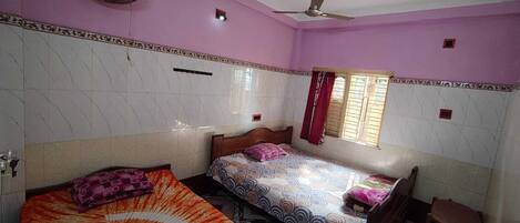 A bedroom with two beds, a ceiling fan, a window with curtains, and a small table.