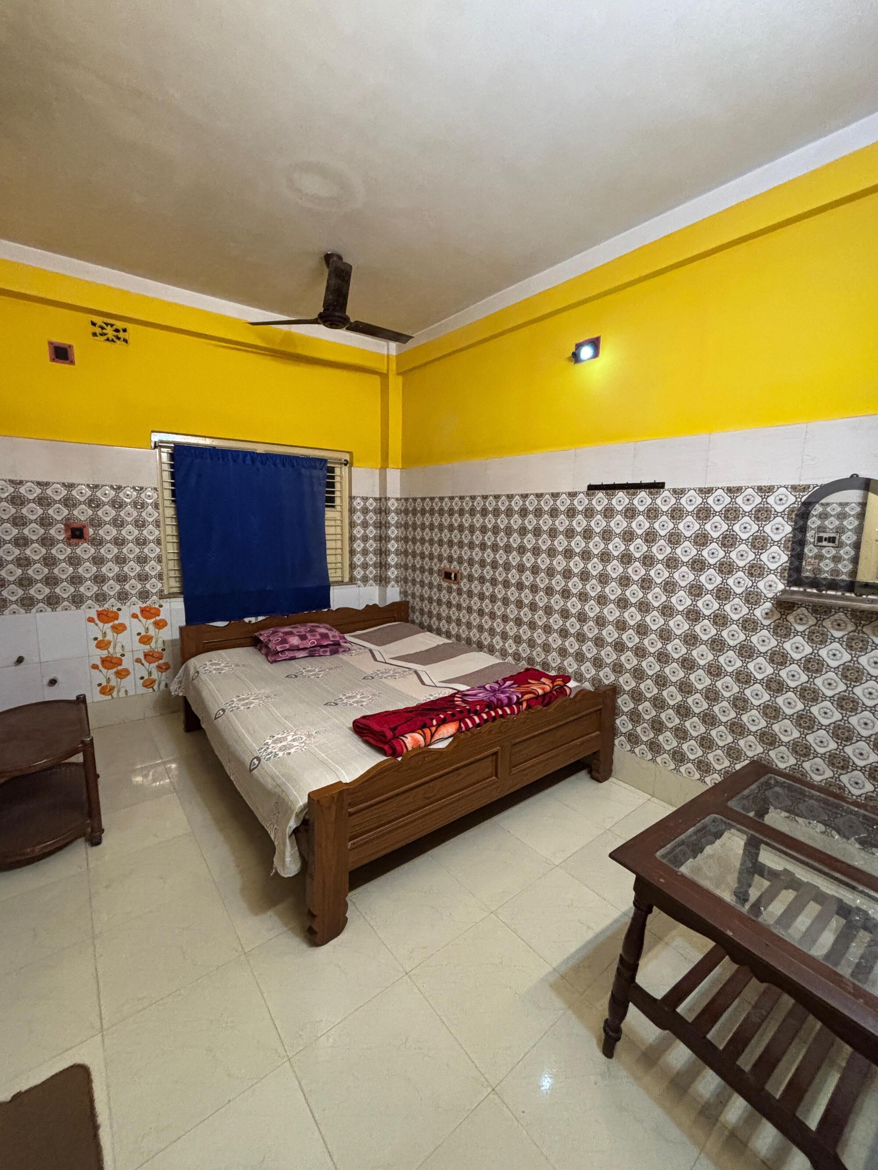 A bedroom with a bed, a chair, a table, and a ceiling fan.