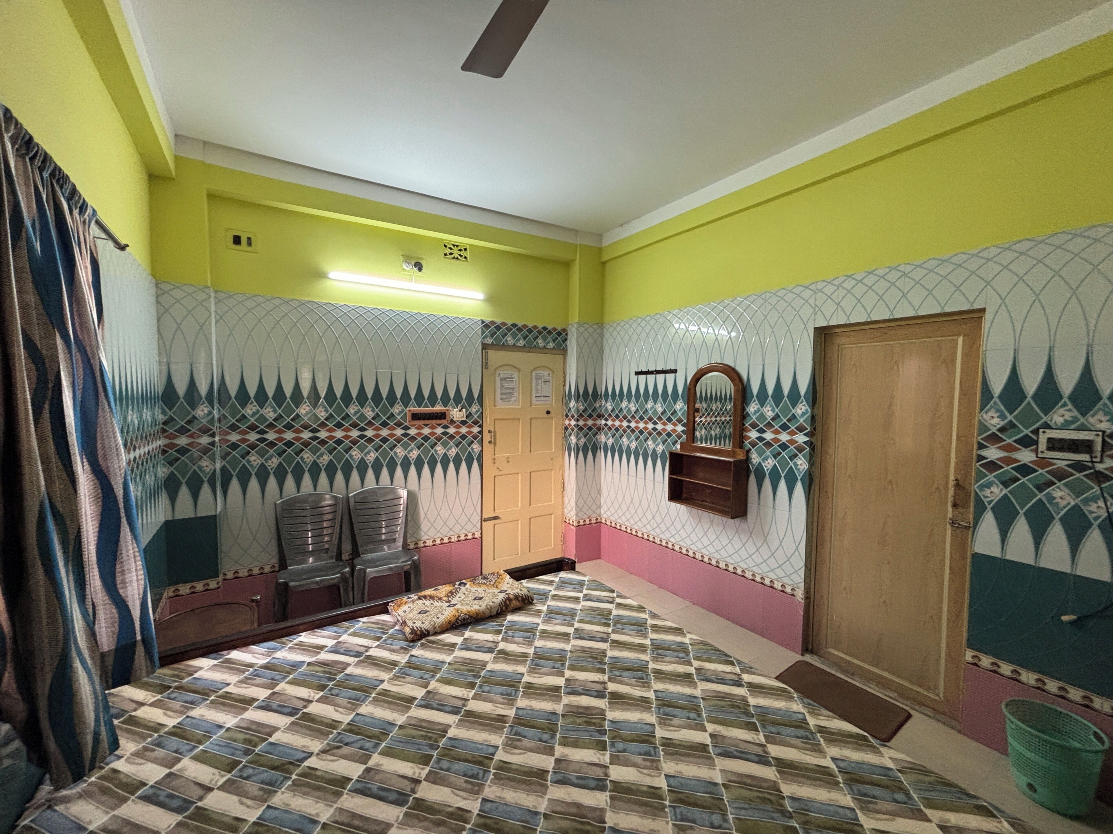 A room with a patterned floor, a bed, a door, and a wall with decorative tiles.