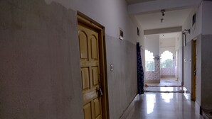 A hallway with a wooden door, white walls, and a tiled floor. - Jagannath Guest House (Krishnanagar)