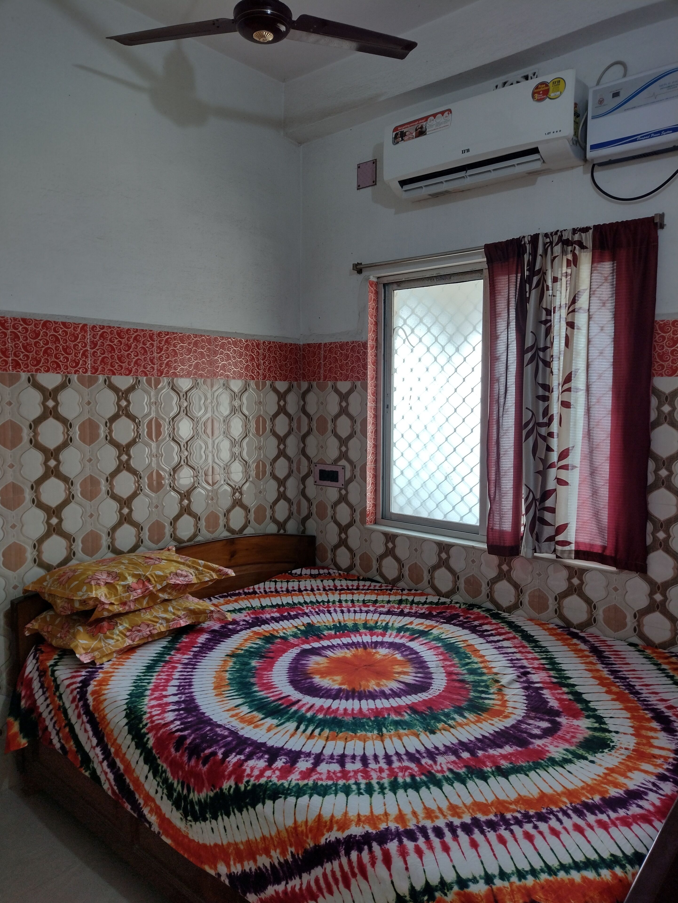 Un dormitorio con una cama, unidad de aire acondicionado, ventana con cortinas y azulejos con diseño.