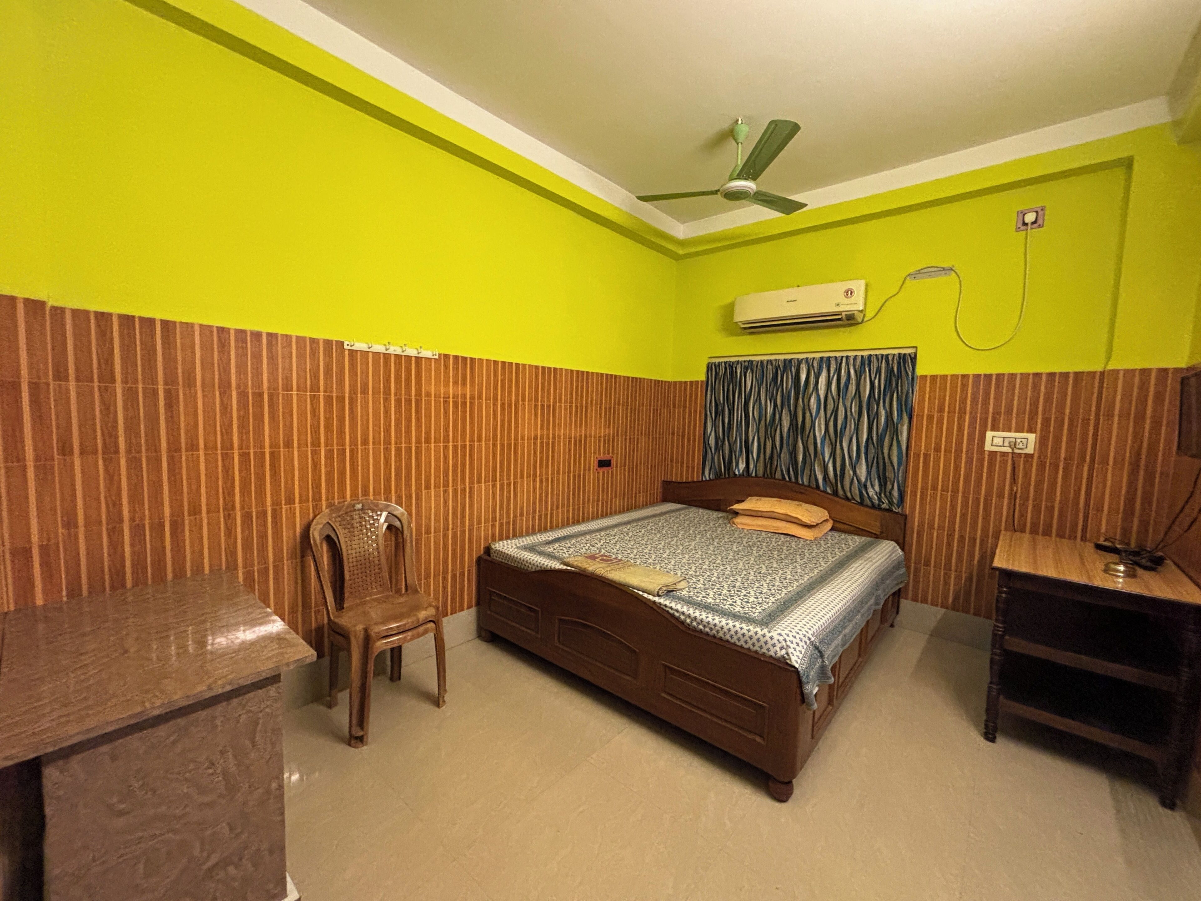 A room with a bed, a chair, a desk, and a ceiling fan.