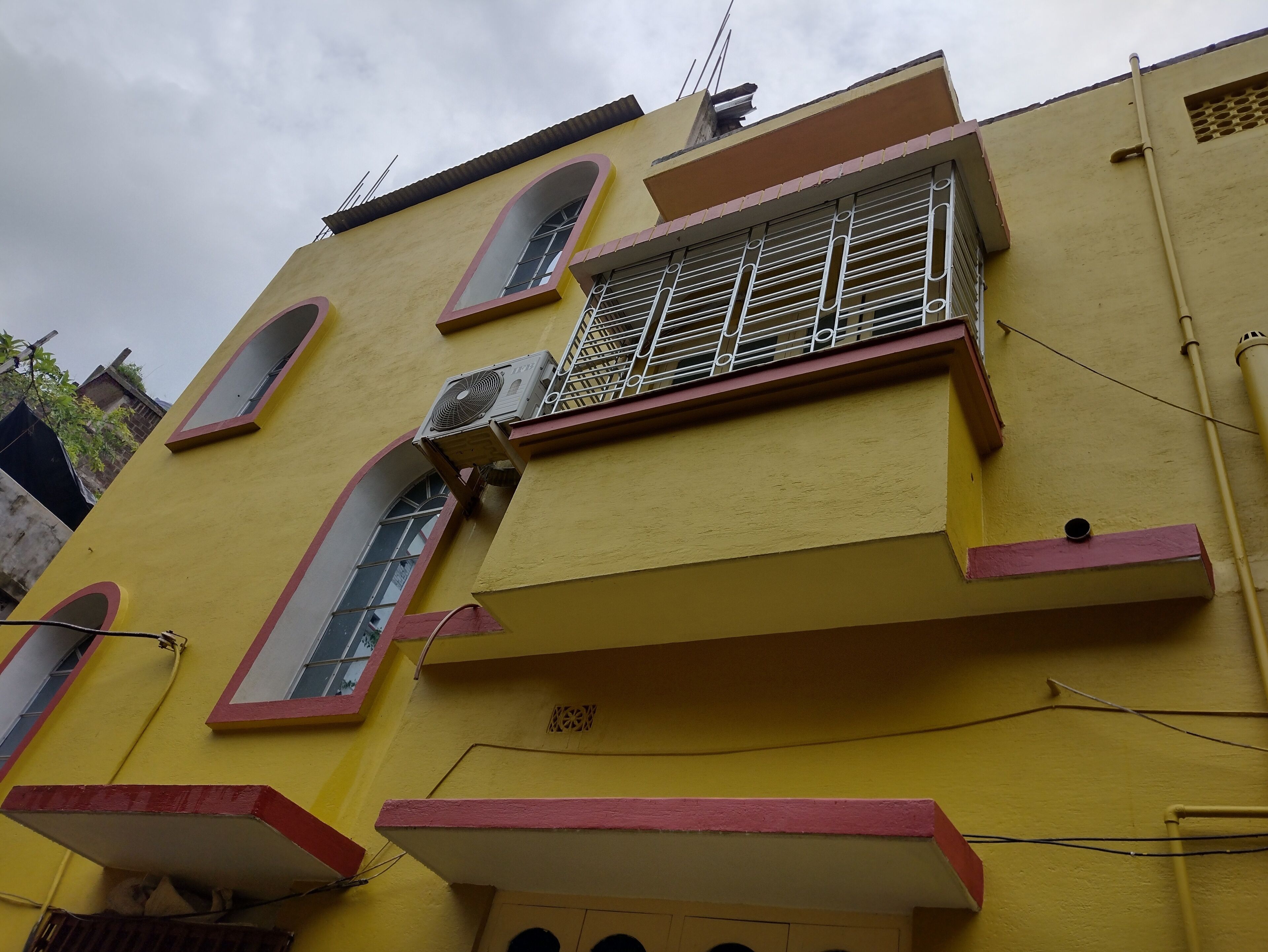 Un bâtiment jaune doté de nombreuses fenêtres, dont une fenêtre grillagée et un ventilateur fixé au mur extérieur.