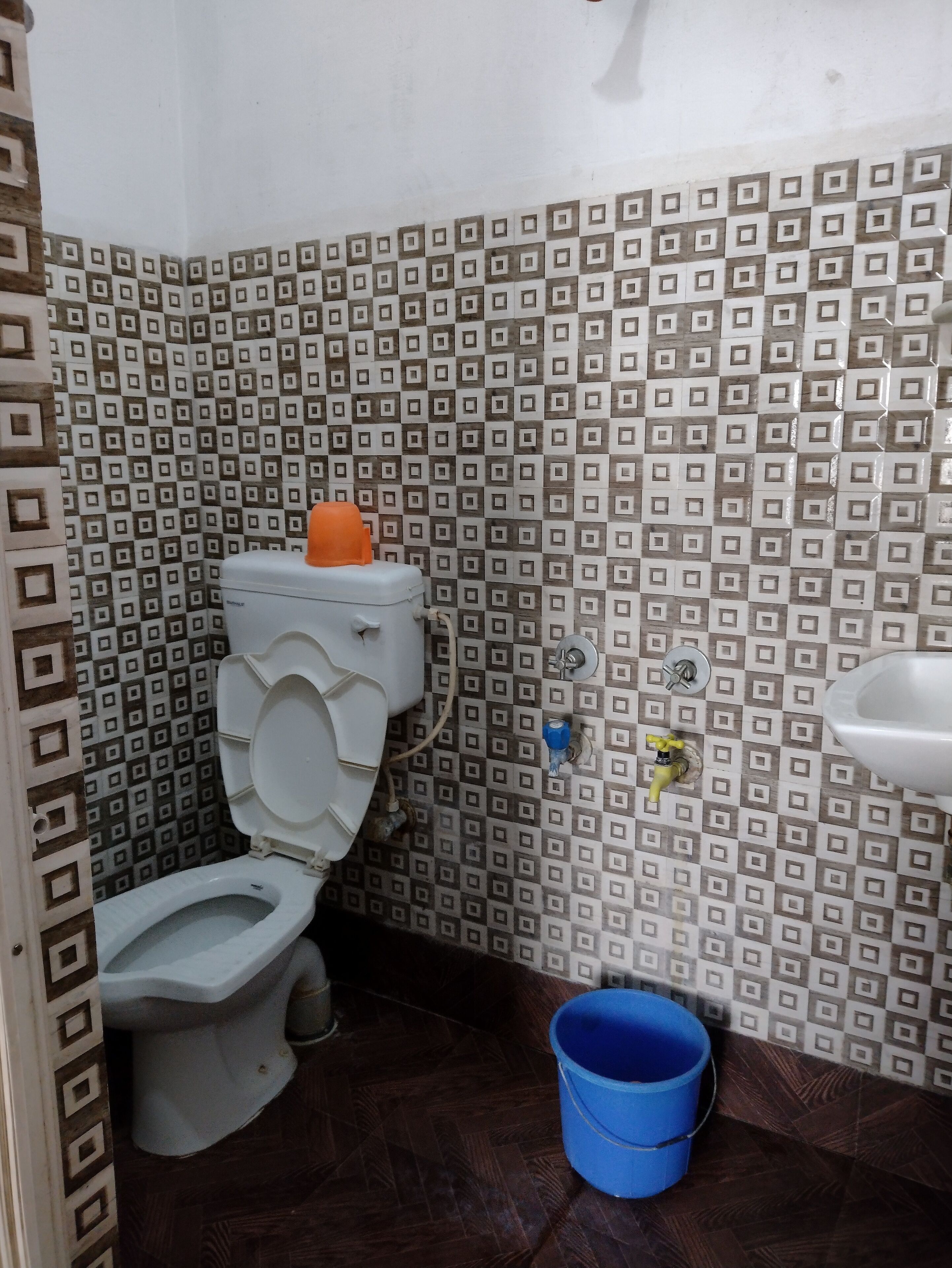 A bathroom with a toilet, a blue bucket, and a patterned wall.
