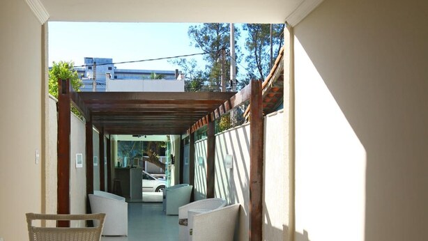 A corridor leading to a covered outdoor seating area with wicker furniture and a view of the street. - MDJ Pousada (Cabo Frio)