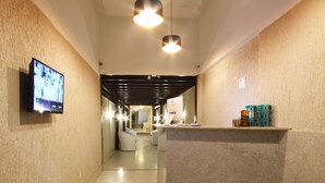 A hotel corridor with a reception desk, a television mounted on the wall, and pendant lighting. - MDJ Pousada (Cabo Frio)