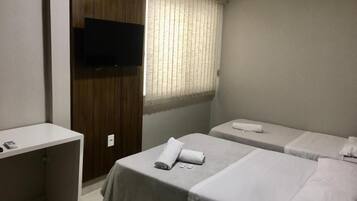 Habitación de hotel con dos camas, un televisor montado en la pared y una ventana con persianas.