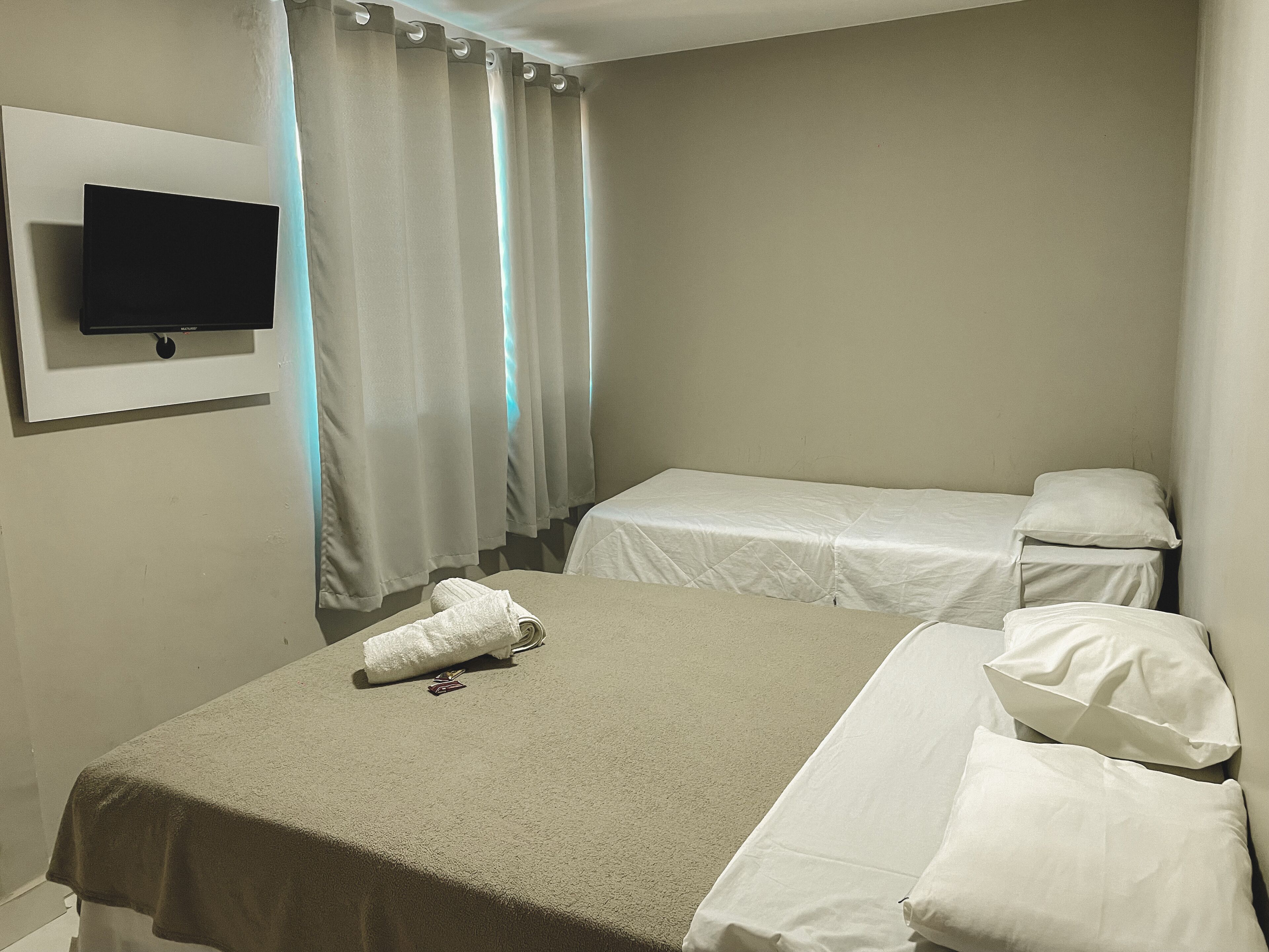 A hotel room with a bed, a TV mounted on the wall, and a window with curtains.