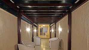 A hallway with wicker chairs, wooden beams, and wall sconces. - MDJ Pousada (Cabo Frio)
