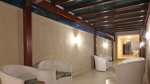 A corridor with wicker chairs and a table, wooden beams on the ceiling, and a light fixture on the wall. - MDJ Pousada (Cabo Frio)