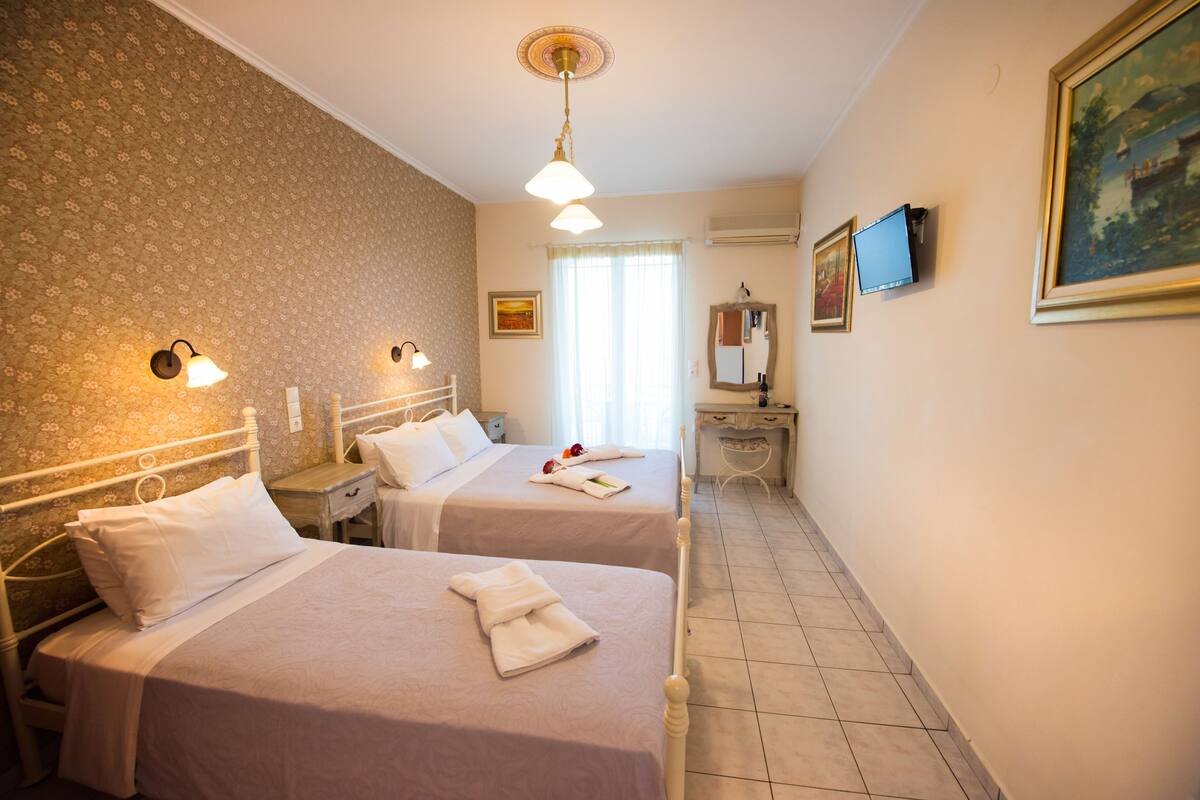 A hotel room with two beds, a desk, a mirror, a television, and a window with curtains.