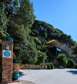 La entrada de un hotel con un muro de piedra, un letrero que dice 'MAISTRO HOTELS' y una escalera que lleva a un edificio con techo amarillo.