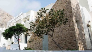 A building with a stone facade and white walls, a tree in front, and a clear sky. - Sail Inn (Santorini)