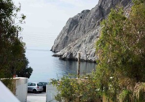 Zona costera con acantilados rocosos, coches estacionados y vegetación.