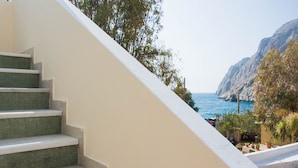 A staircase leading to a balcony overlooking a coastal area with a view of the sea and rocky cliffs. - Sail Inn (Santorini)