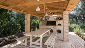 Un patio al aire libre con chimenea de ladrillo, bancos de madera y lámparas colgantes.