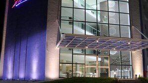 Un hotel moderno con un llamativo letrero de neón, grandes ventanales y un área de entrada cubierta.
