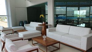 Un moderno vestíbulo de hotel con sofás blancos, una mesa de centro de madera y un jarrón con flores amarillas.
