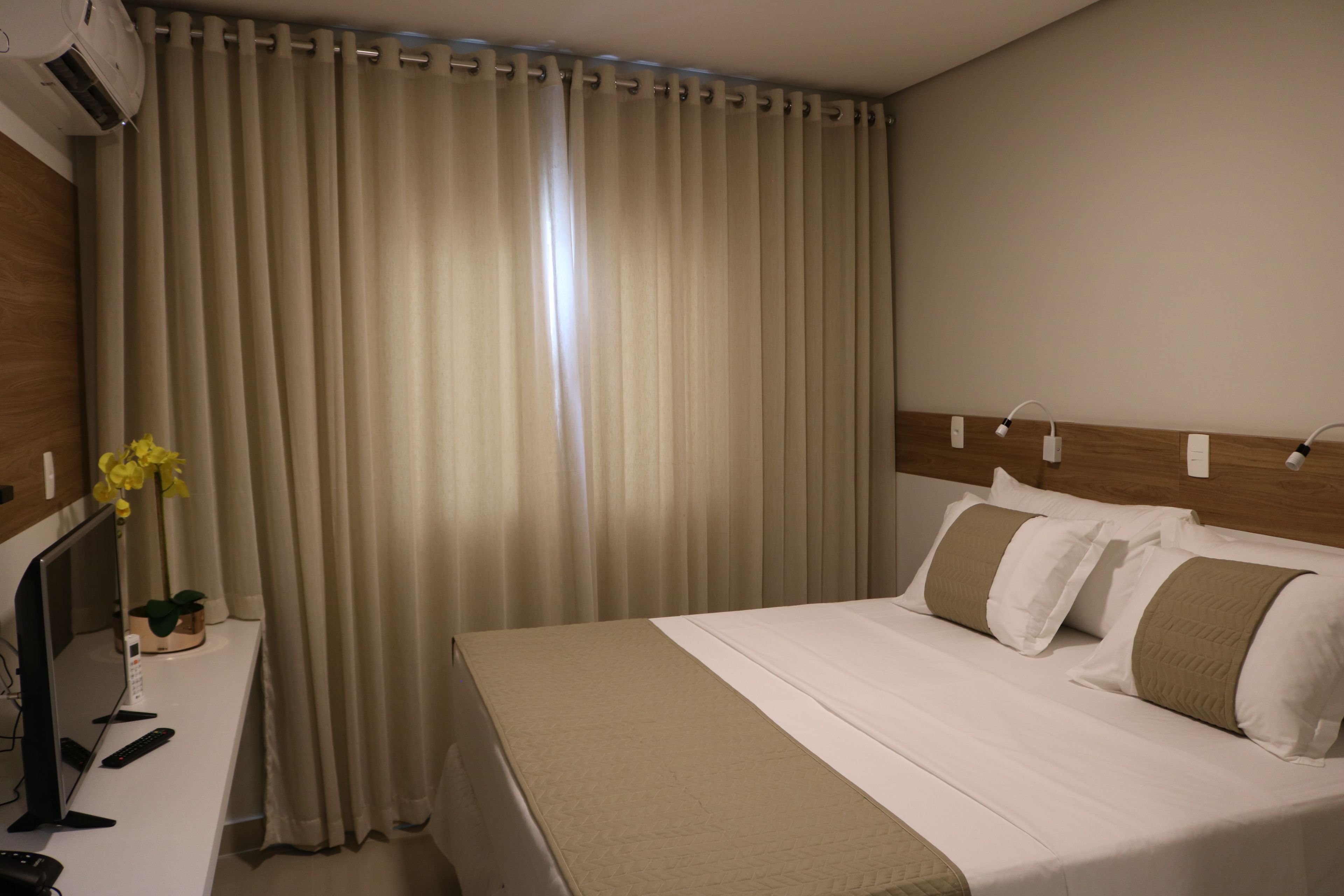 A hotel room with a bed, a desk with a computer, a lamp, and a plant.