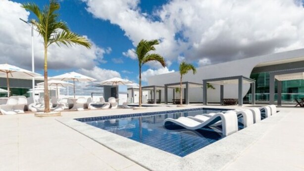 Un área de piscina moderna con sillones de descanso, sombrillas y palmeras.