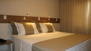 Una habitación de hotel con una cama bien hecha, una mesita de noche con lámpara y un enchufe en la pared.