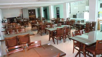 A spacious restaurant with multiple dining tables and chairs, a kitchen area, and a reception desk.