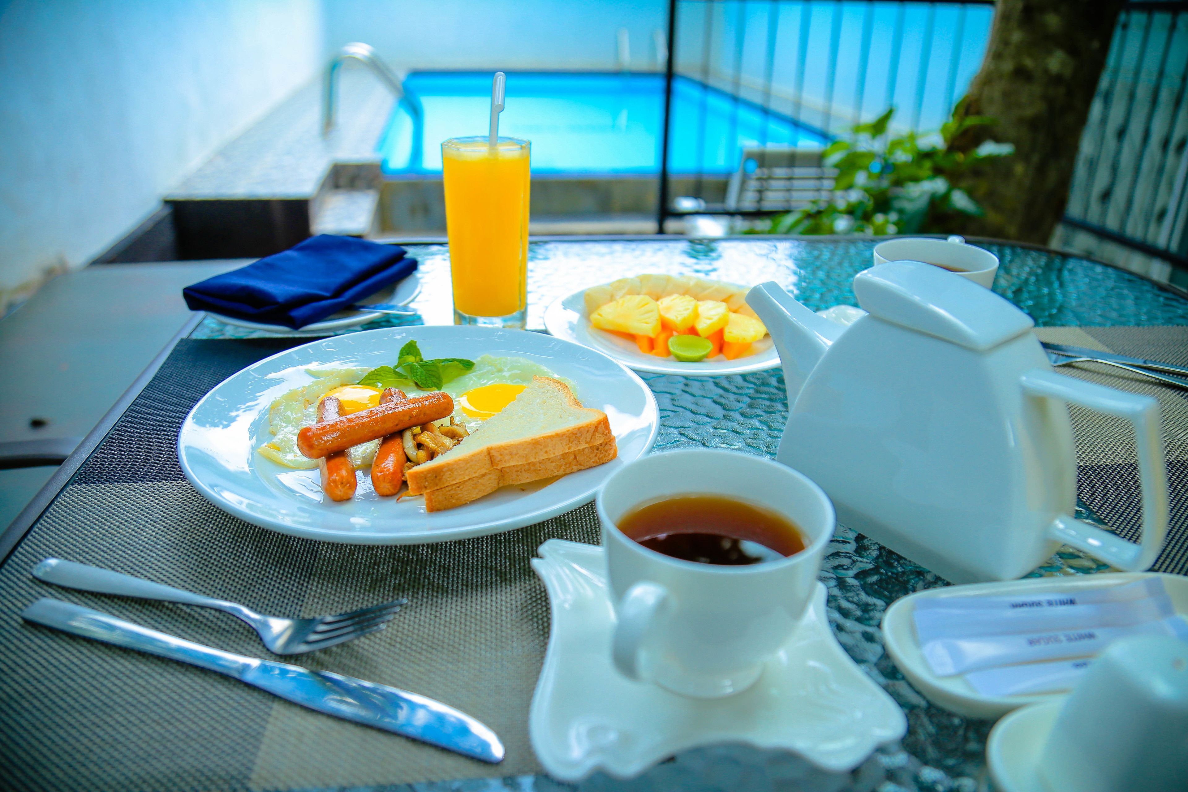 Escena de desayuno con vista a la piscina, incluyendo platos de comida, una bebida y productos para el desayuno.