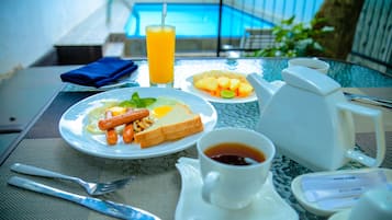 Escena de desayuno con vista a la piscina, incluyendo platos de comida, una bebida y productos para el desayuno.