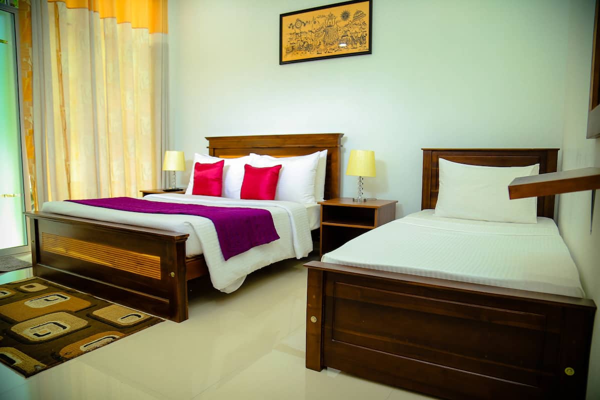 A hotel room with two wooden beds, a nightstand, a lamp, and a window with curtains.