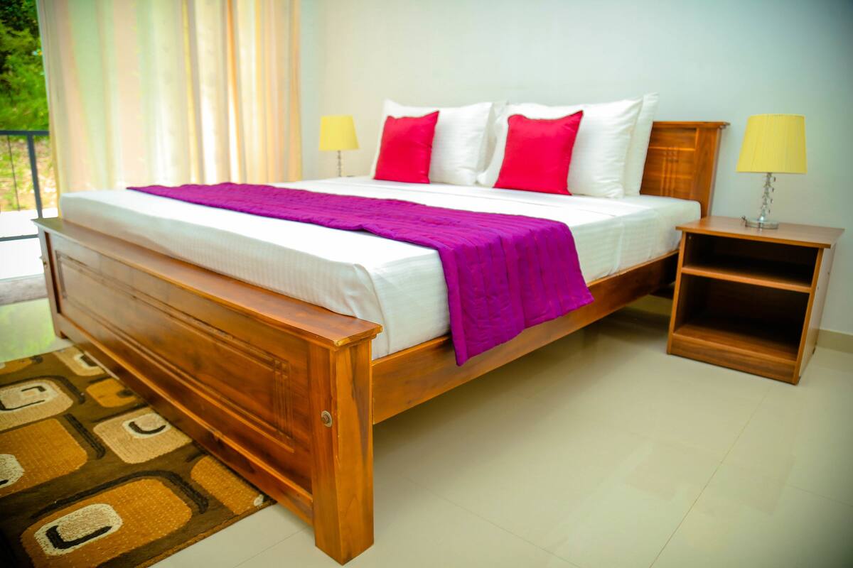 A wooden bed with a purple blanket, white and red pillows, and two bedside lamps.