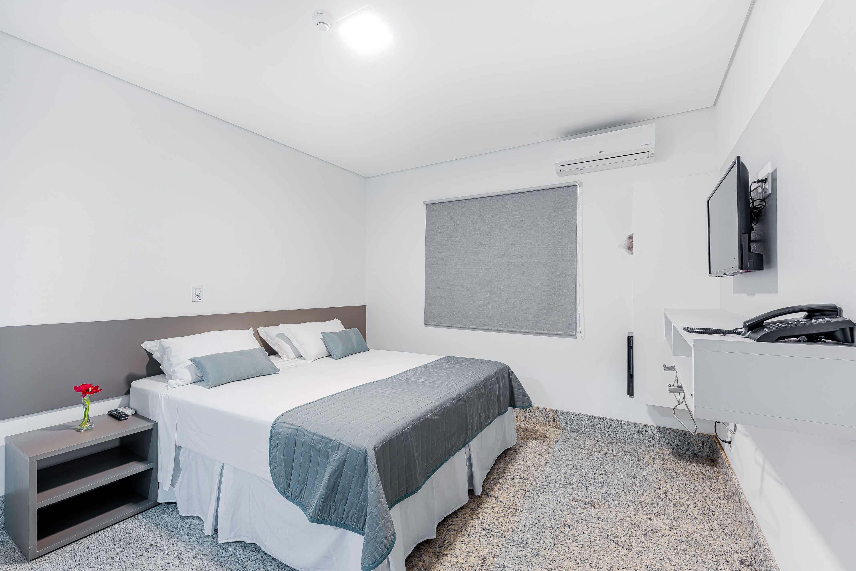 A modern hotel room with a bed, bedside table, and a TV mounted on the wall.