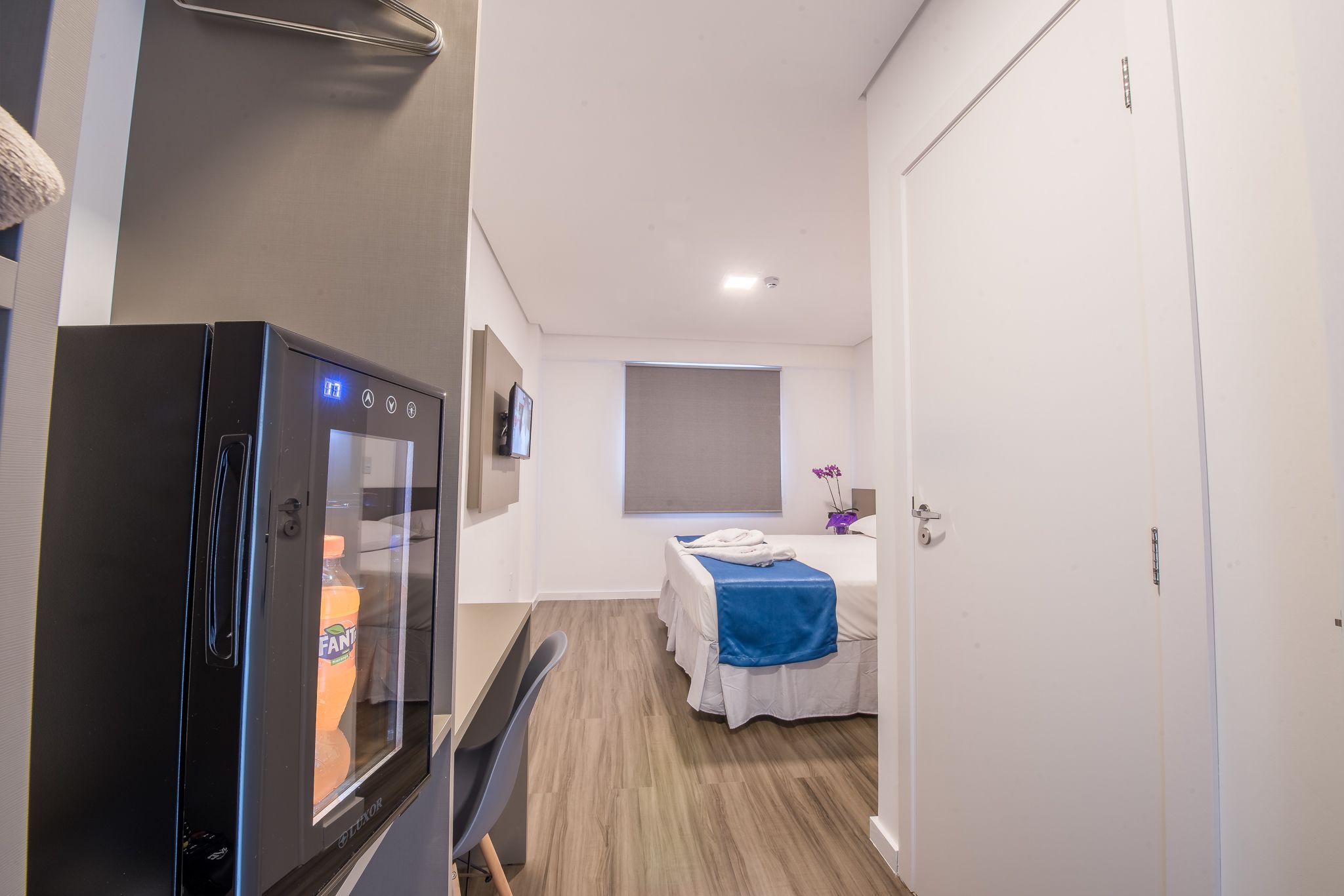 Habitación de hotel con cama, escritorio pequeño, refrigerador y ventana.