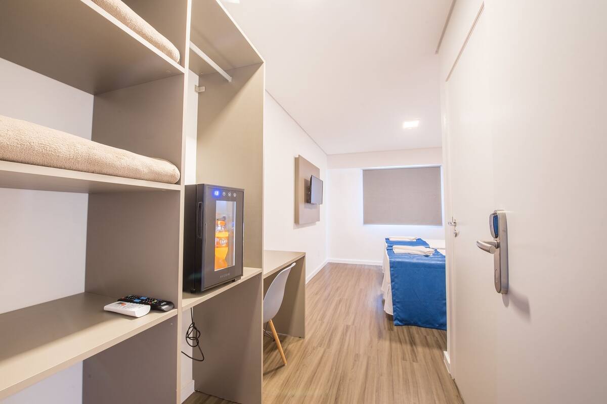 A hotel room with a bed, a desk, a TV, and a minibar.