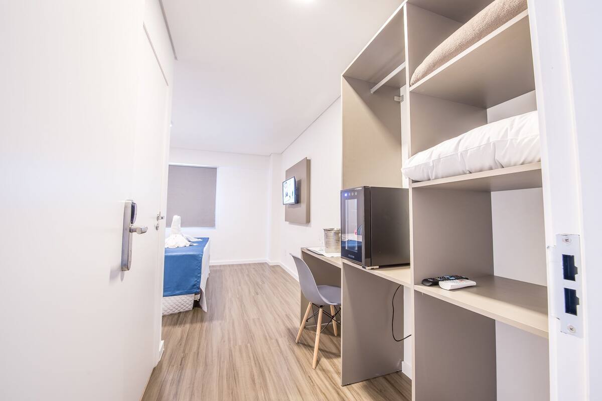 A compact hotel room with a bed, desk, and built-in wardrobe.