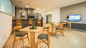 A modern kitchen with wooden chairs, a dining table, and a television displaying a menu. - Prime Hotel Ponta Porã (Ponta Pora)