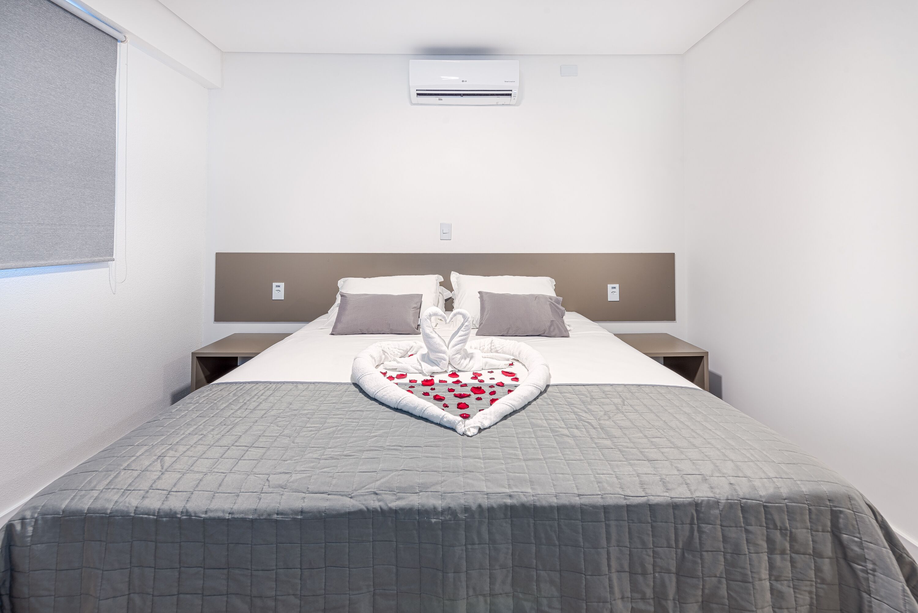 A hotel room with a bed, a headboard, a bedside table, and an air conditioning unit.