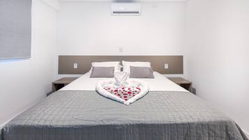 A hotel room with a bed, a headboard, a bedside table, and an air conditioning unit.