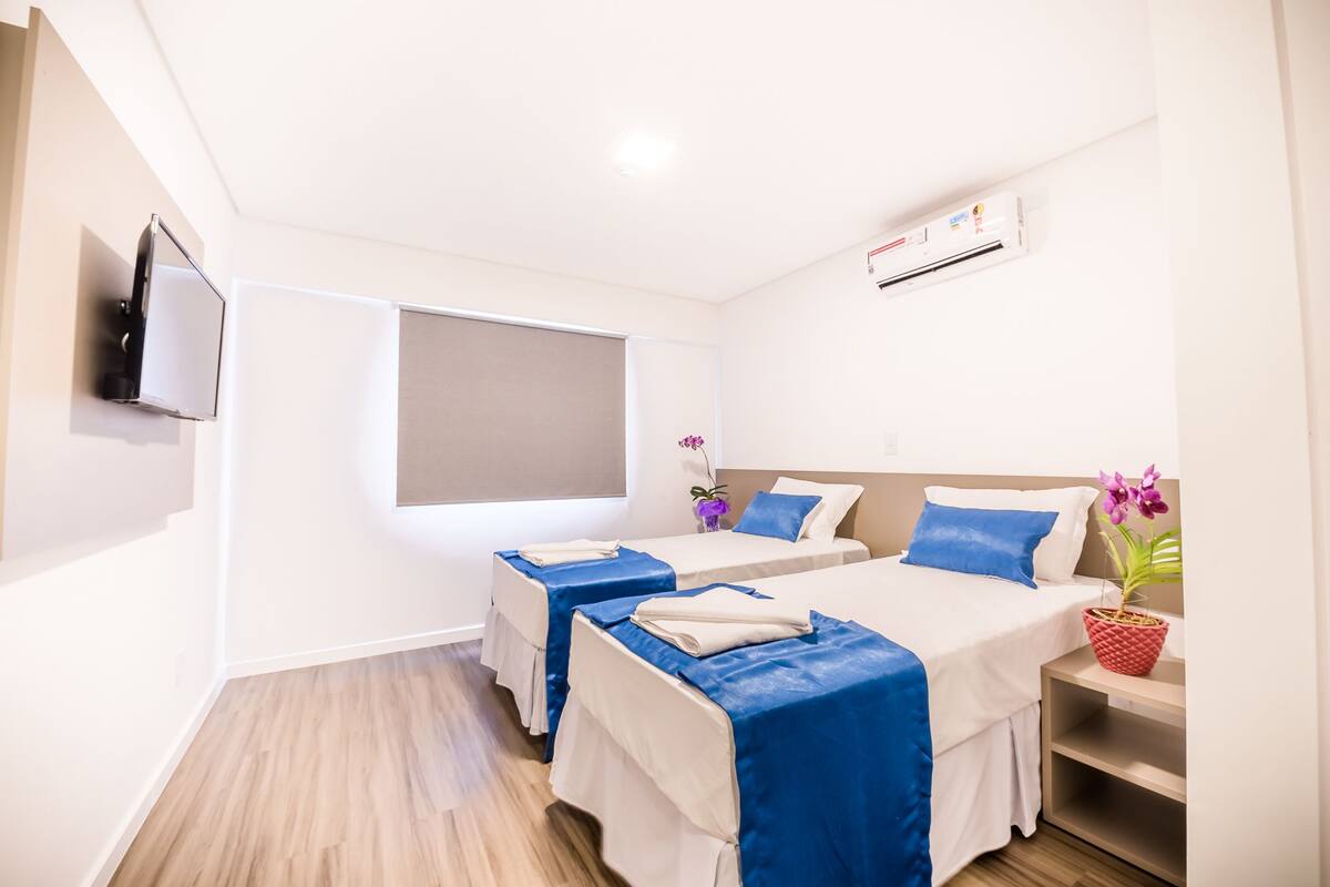 A hotel room with two beds, a TV, an air conditioner, and a window.