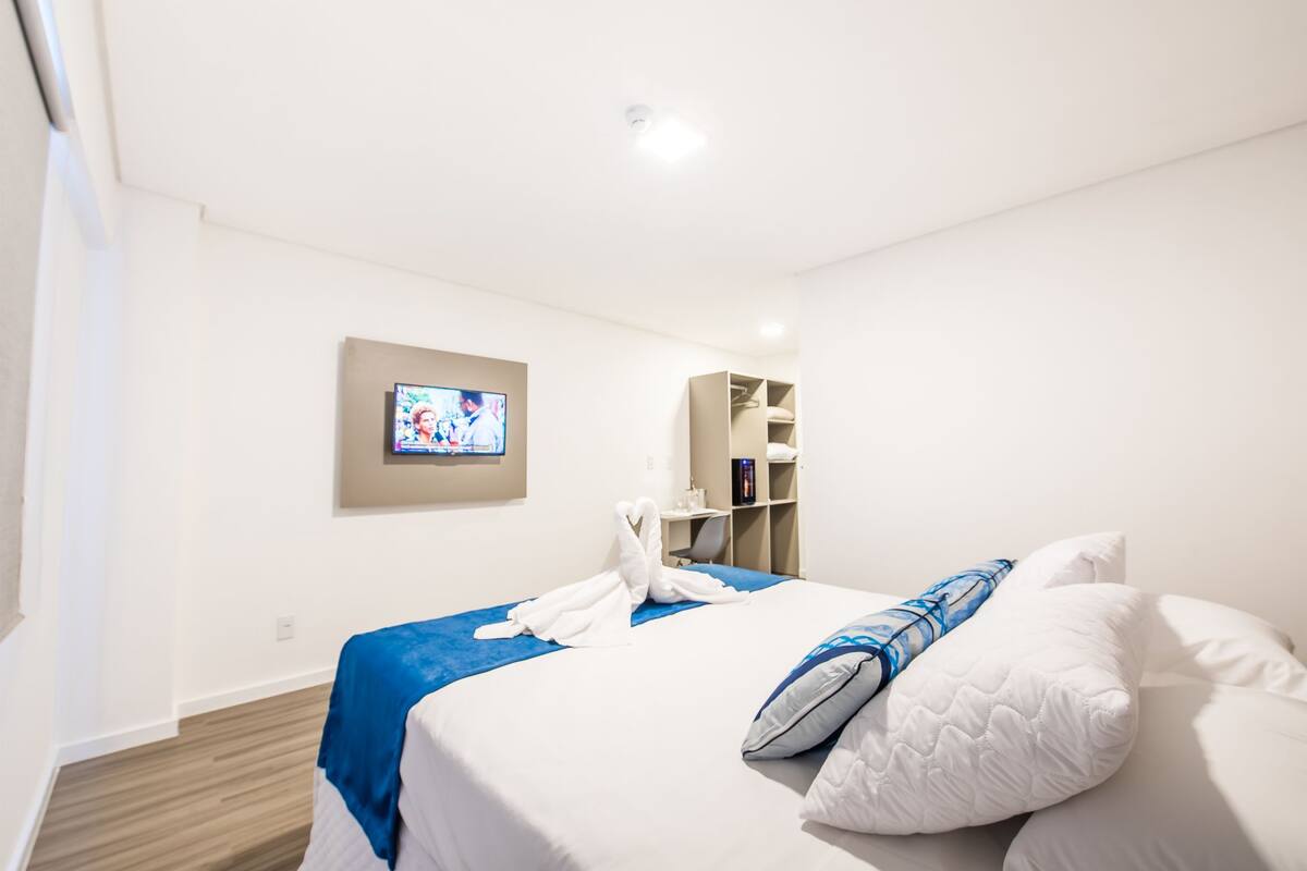 A hotel room with a bed, a TV mounted on the wall, a desk, and a wardrobe.