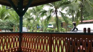 A view from a covered area with a wooden lattice fence, palm trees, and a building in the background.