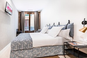 Ein modernes Schlafzimmer mit Bett, Nachttisch mit Zeitschrift, Wand-TV und Blick auf den Balkon.