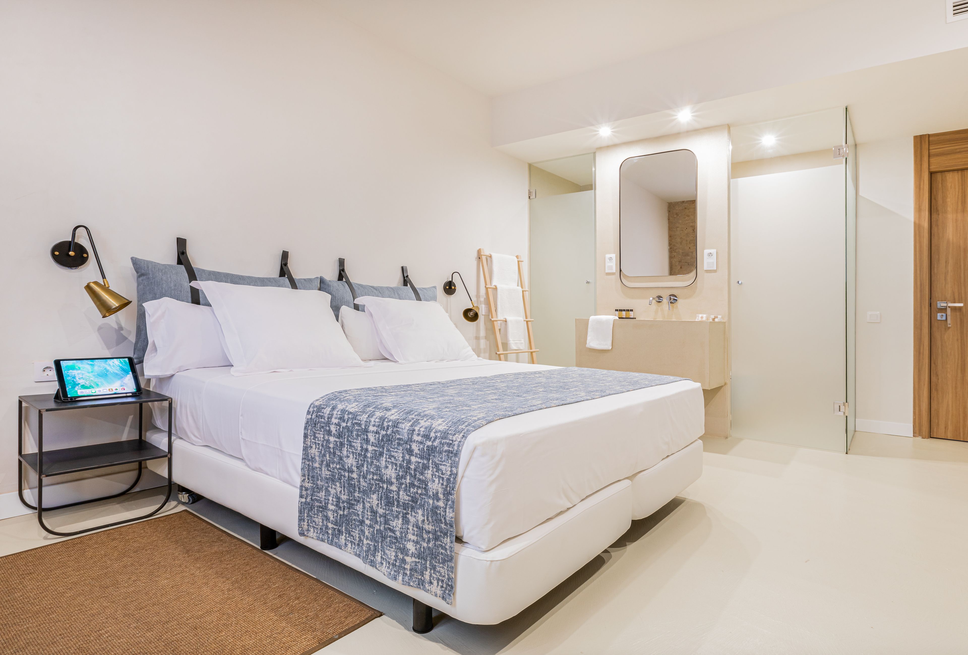 A modern bedroom with a bed, bedside table, lamp, and a mirror above the sink.