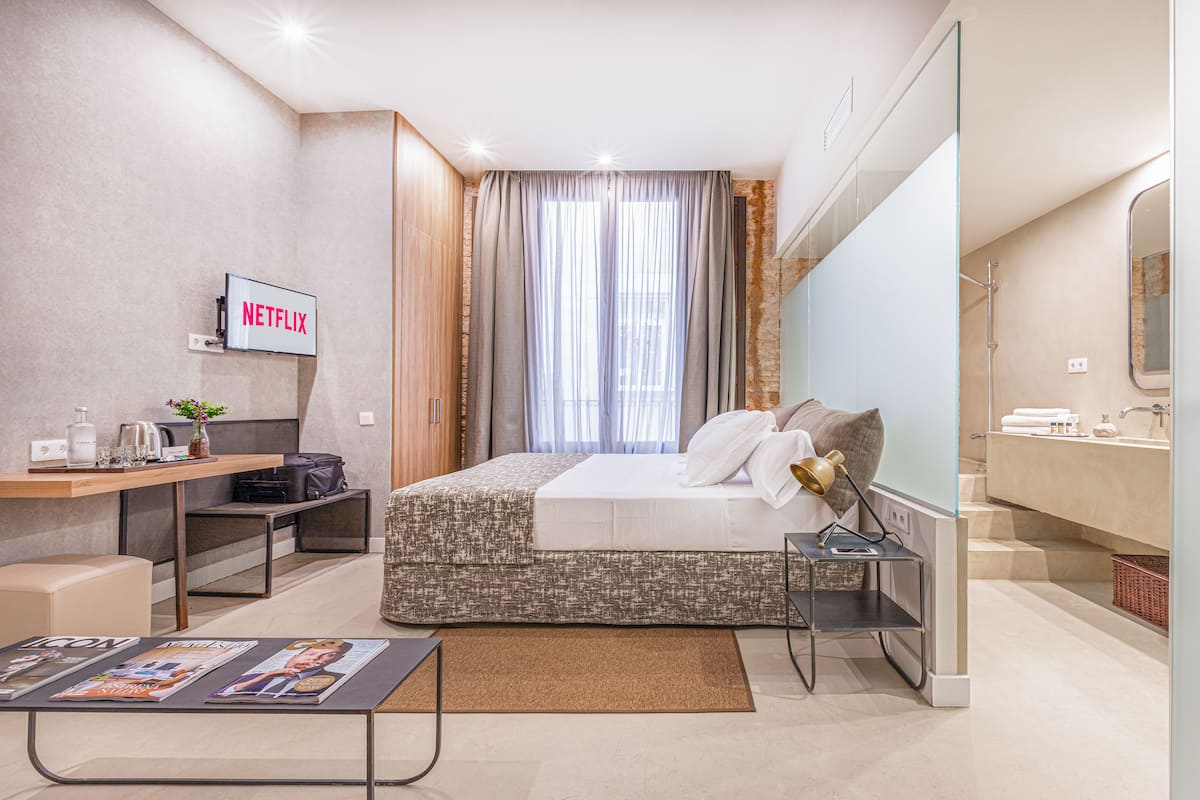 Ein modernes Hotelzimmer mit Bett, Nachttisch, Fernseher und Schreibtisch mit Computer.